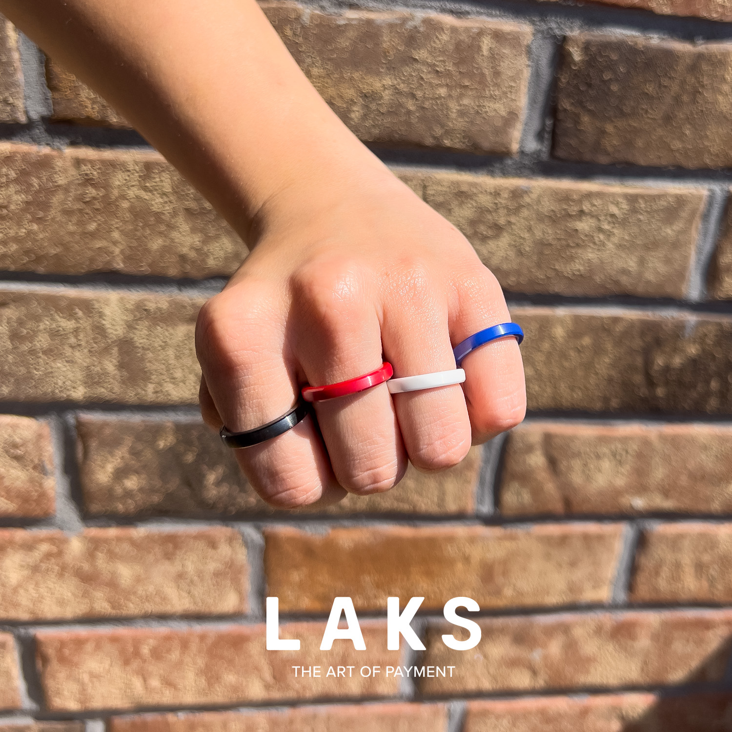 hand mit Bezahlringen in schwarz, rot, weiß und blau an den Fingern und Schriftzug Laks untenmittig