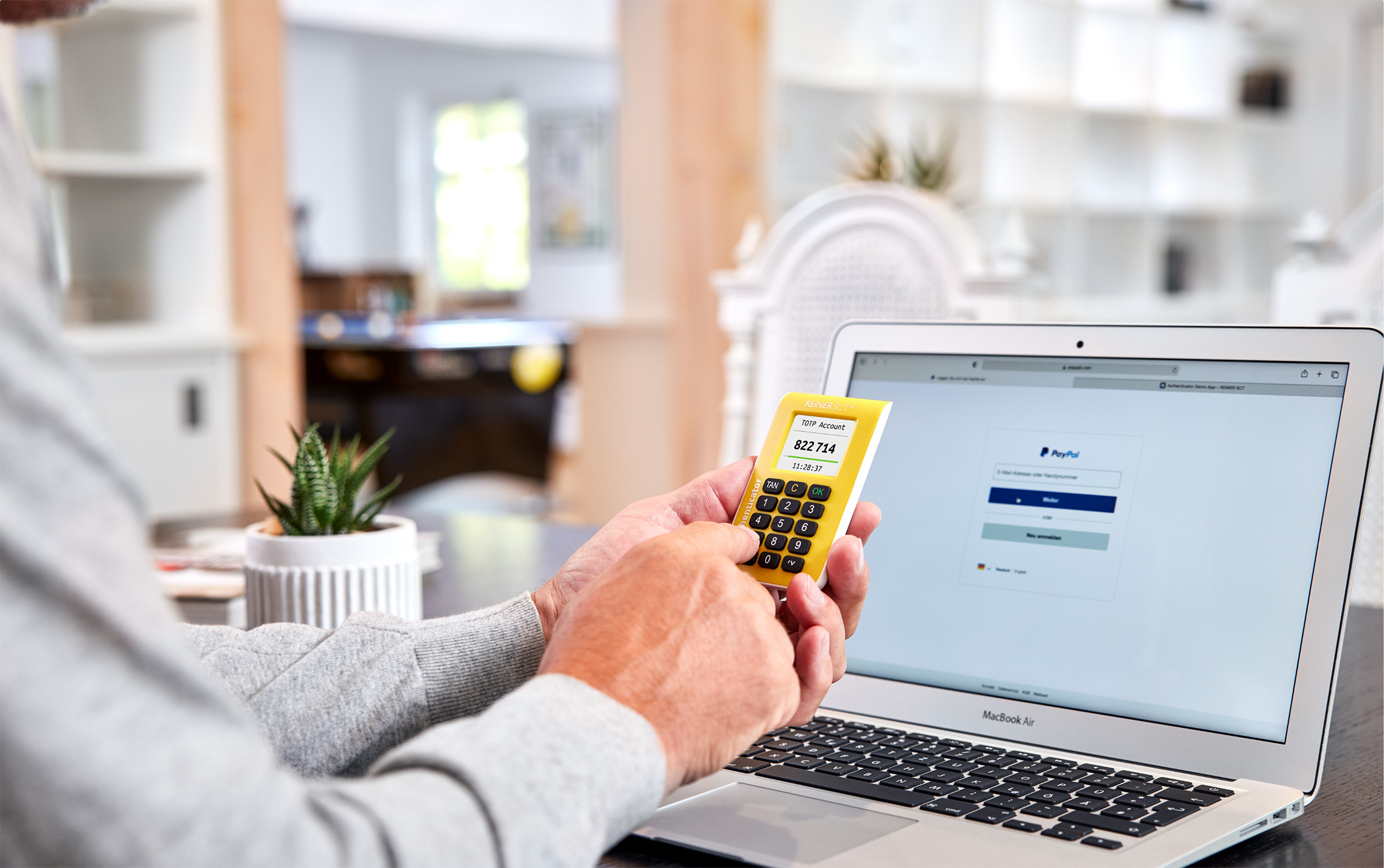 Reiner SCT Authenticator in einer Hand vor einem Rechner